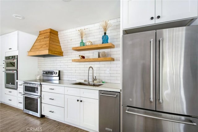 kitchen with custom exhaust hood, white cabinets, sink, appliances with stainless steel finishes, and dark hardwood / wood-style flooring