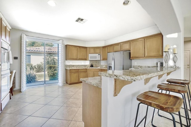 kitchen featuring a kitchen breakfast bar, backsplash, kitchen peninsula, stainless steel fridge, and light tile patterned floors