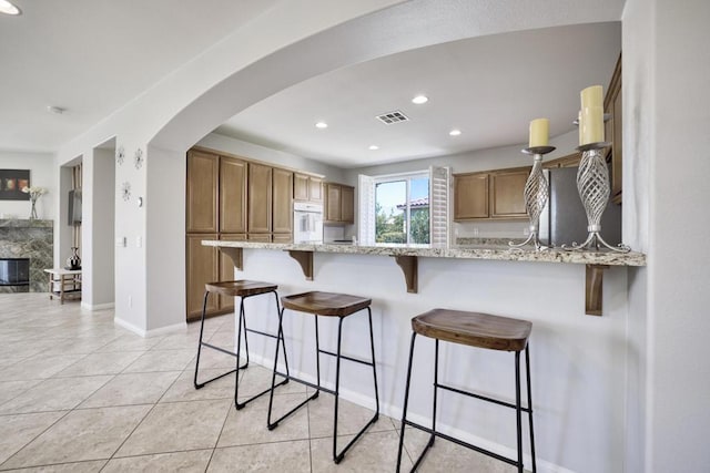 kitchen with light stone countertops, a breakfast bar, white oven, a premium fireplace, and light tile patterned flooring