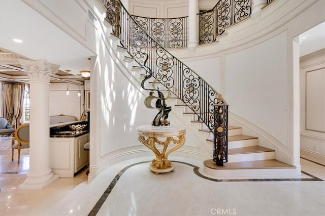 stairway with decorative columns, a decorative wall, and a high ceiling