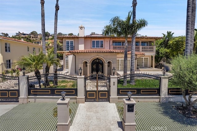 mediterranean / spanish-style home featuring a balcony, a tile roof, a fenced front yard, stucco siding, and french doors