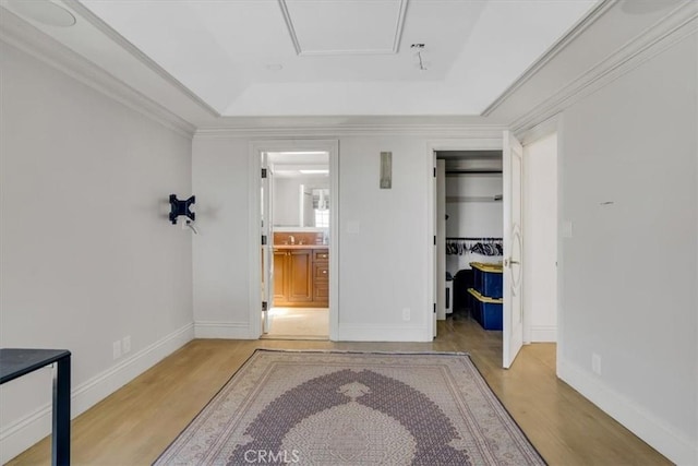 interior space with baseboards, a tray ceiling, wood finished floors, and crown molding