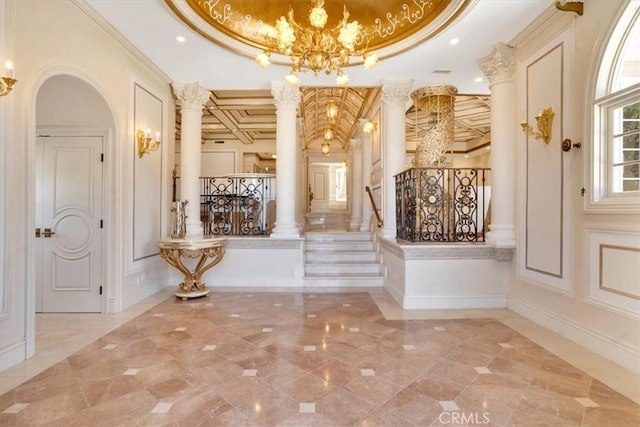 corridor featuring a decorative wall, crown molding, stairs, decorative columns, and an inviting chandelier