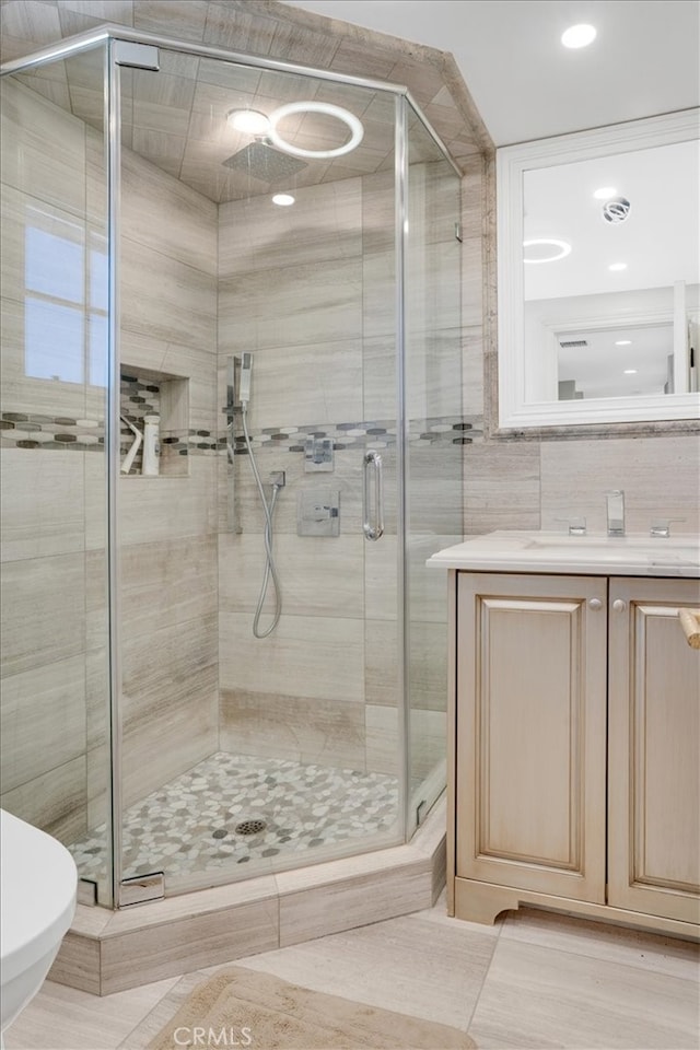 bathroom with tile walls, a shower with door, tile patterned floors, vanity, and toilet