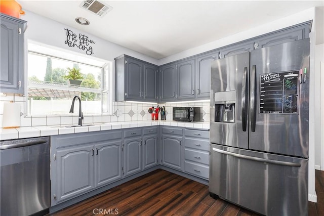 kitchen featuring stainless steel appliances, gray cabinetry, decorative backsplash, dark wood-type flooring, and sink