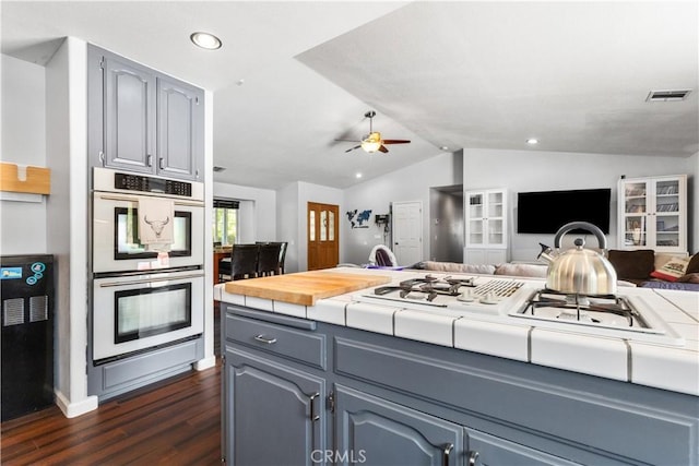 kitchen featuring dark hardwood / wood-style floors, gray cabinets, vaulted ceiling, ceiling fan, and multiple ovens