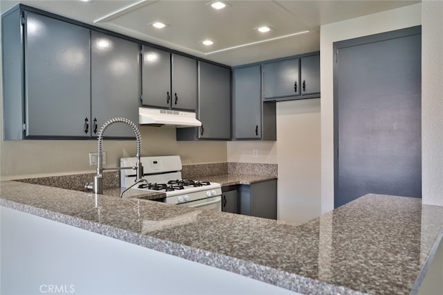 kitchen with dark stone counters, kitchen peninsula, white gas range oven, and gray cabinets