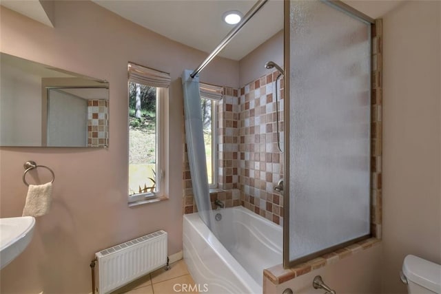 bathroom featuring tile patterned flooring, toilet, tiled shower / bath, and radiator