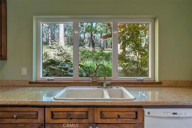 kitchen featuring dishwasher, light stone countertops, a wealth of natural light, and sink