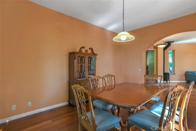 dining room featuring arched walkways, wood finished floors, and baseboards