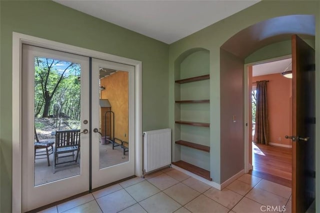doorway to outside featuring built in features, french doors, light tile patterned flooring, radiator heating unit, and arched walkways