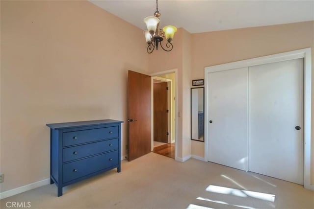 unfurnished bedroom featuring light carpet, a notable chandelier, a closet, and baseboards