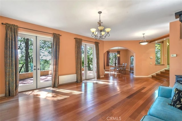 unfurnished living room with radiator heating unit, french doors, an inviting chandelier, and hardwood / wood-style flooring