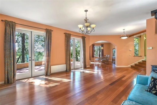 unfurnished living room featuring french doors, radiator heating unit, arched walkways, and a healthy amount of sunlight