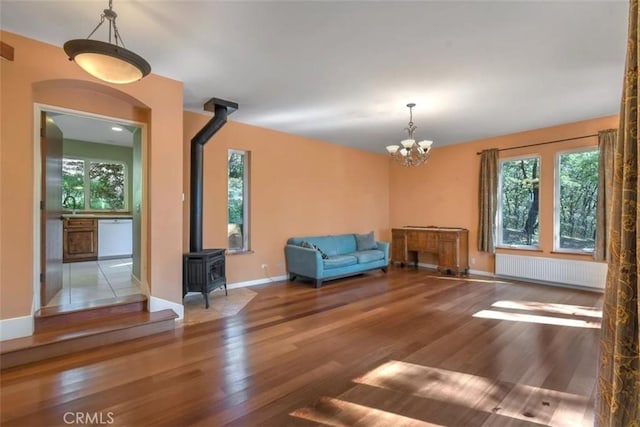 unfurnished room featuring a wood stove, radiator, plenty of natural light, and wood finished floors