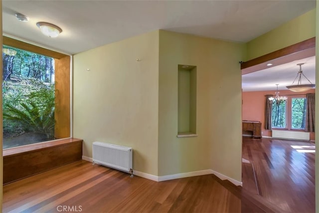 spare room with a notable chandelier, wood-type flooring, and radiator heating unit