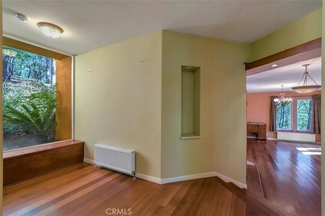 unfurnished room with radiator heating unit, a chandelier, wood finished floors, and baseboards