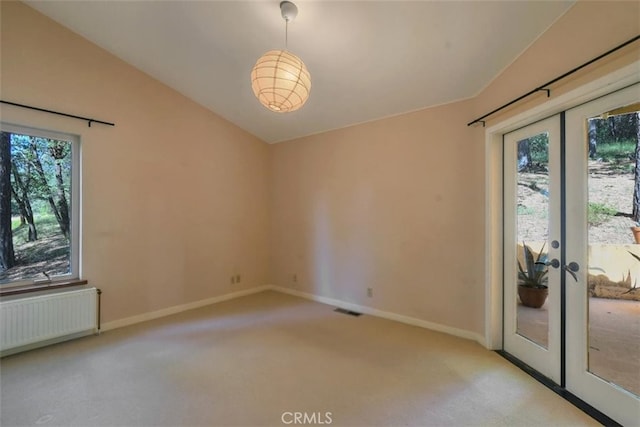 empty room featuring vaulted ceiling, radiator heating unit, light colored carpet, and french doors