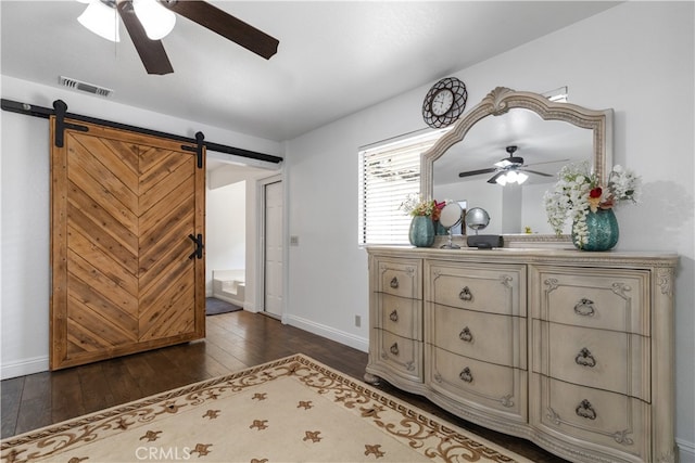 interior space with a barn door, ceiling fan, and dark wood-type flooring