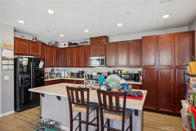 kitchen with appliances with stainless steel finishes, a center island with sink, light hardwood / wood-style floors, and a kitchen breakfast bar