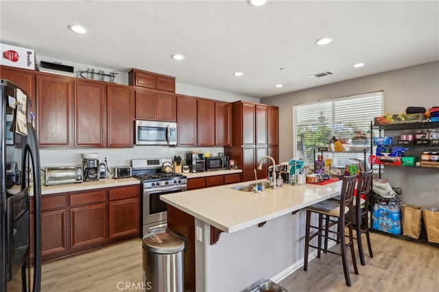 kitchen with sink, light hardwood / wood-style flooring, stainless steel appliances, and a breakfast bar