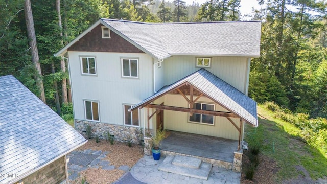view of front of property featuring a shingled roof, stone siding, and a view of trees