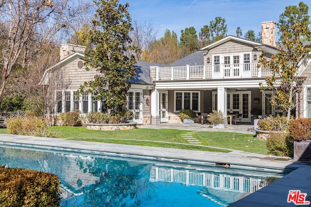 rear view of house featuring a lawn, a balcony, a patio area, and french doors