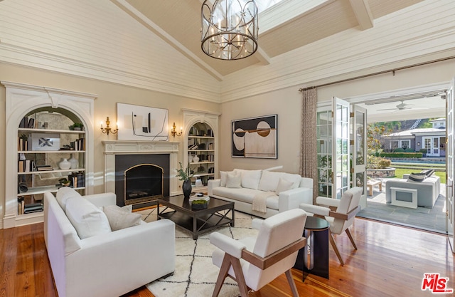 living room featuring hardwood / wood-style flooring, ceiling fan with notable chandelier, built in features, and high vaulted ceiling