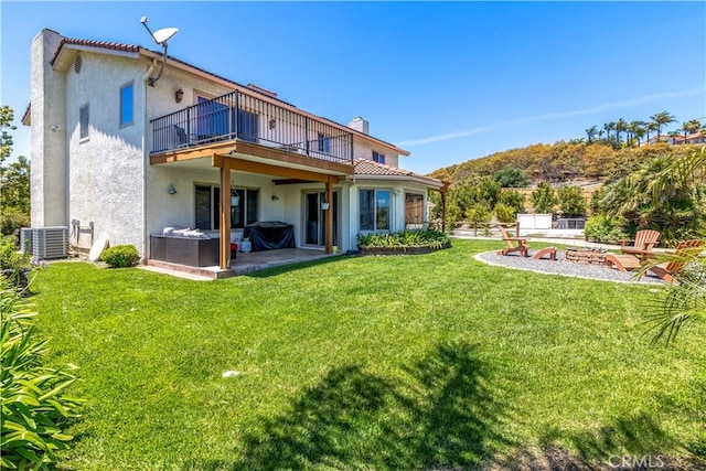 back of property with a balcony, a patio, cooling unit, a yard, and a hot tub