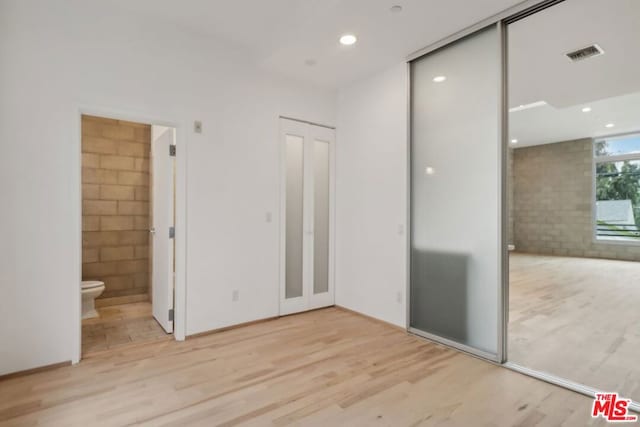 unfurnished bedroom featuring a closet, ensuite bathroom, and light hardwood / wood-style flooring