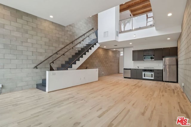 unfurnished living room featuring light hardwood / wood-style floors, tile walls, and a high ceiling