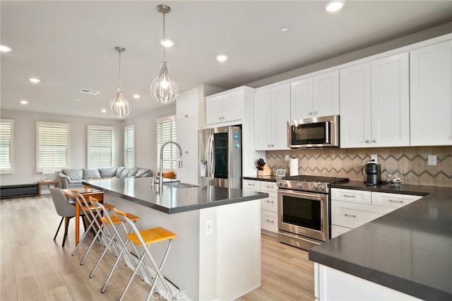 kitchen featuring a kitchen island with sink, stainless steel appliances, sink, a kitchen bar, and pendant lighting