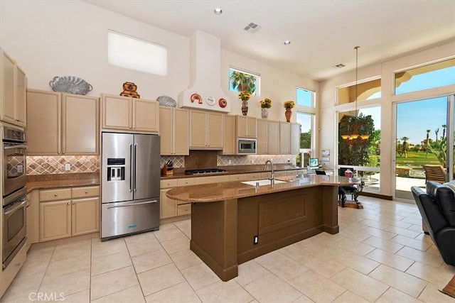 kitchen with sink, appliances with stainless steel finishes, a kitchen island with sink, a high ceiling, and decorative backsplash