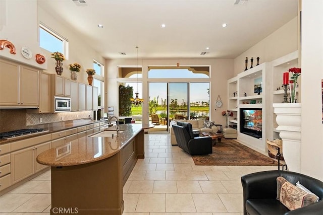 kitchen featuring appliances with stainless steel finishes, tasteful backsplash, sink, light stone countertops, and a center island with sink