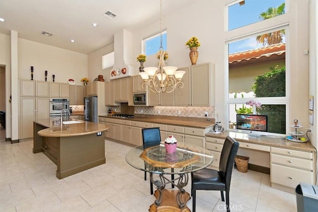 kitchen featuring sink, tasteful backsplash, a center island with sink, a towering ceiling, and stainless steel appliances