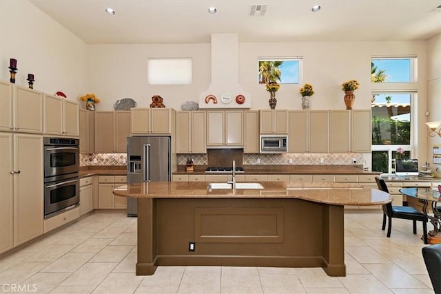 kitchen with appliances with stainless steel finishes, sink, light stone countertops, and an island with sink