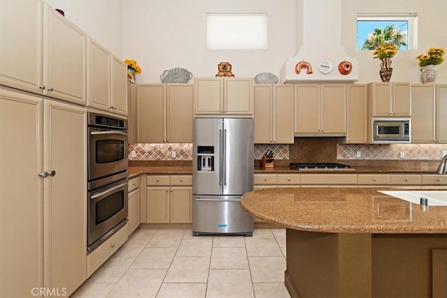 kitchen featuring a high ceiling, cream cabinetry, backsplash, and appliances with stainless steel finishes