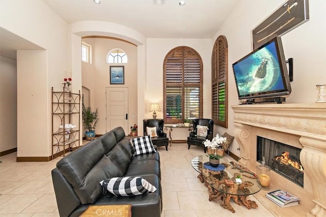 living area featuring tile patterned flooring, a fireplace, baseboards, and a towering ceiling