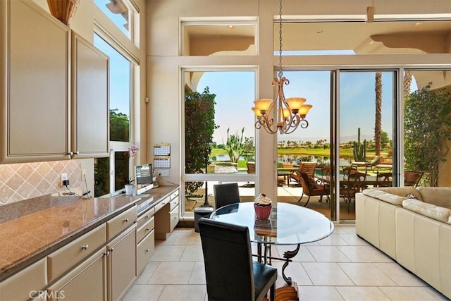 kitchen featuring light stone counters, an inviting chandelier, light tile patterned floors, pendant lighting, and decorative backsplash