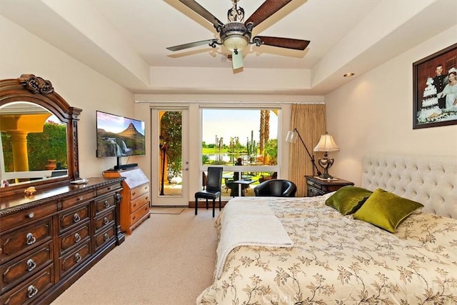 bedroom featuring a tray ceiling, light colored carpet, a ceiling fan, and access to outside