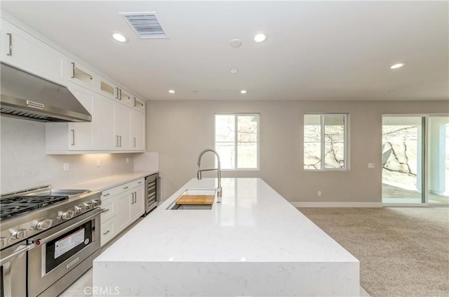 kitchen featuring sink, wine cooler, ventilation hood, double oven range, and a center island with sink