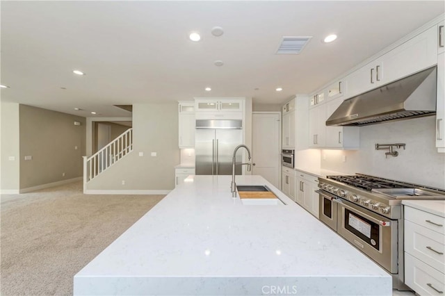 kitchen with light carpet, white cabinets, sink, an island with sink, and premium appliances