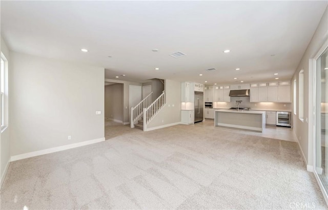 unfurnished living room with sink, light carpet, and wine cooler