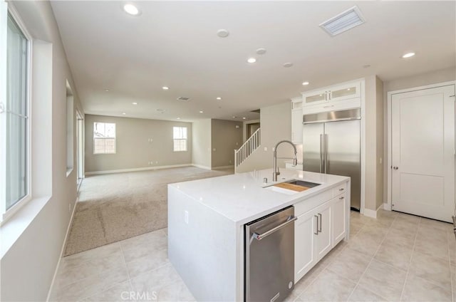 kitchen with appliances with stainless steel finishes, sink, a center island with sink, white cabinets, and light tile patterned flooring