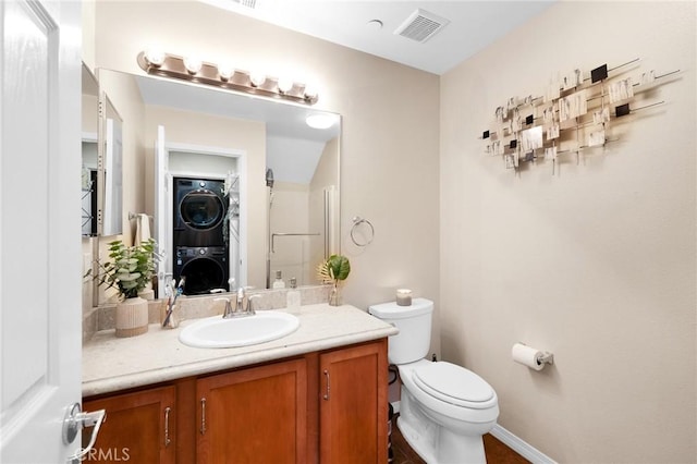 bathroom with toilet, visible vents, vanity, baseboards, and stacked washer and clothes dryer