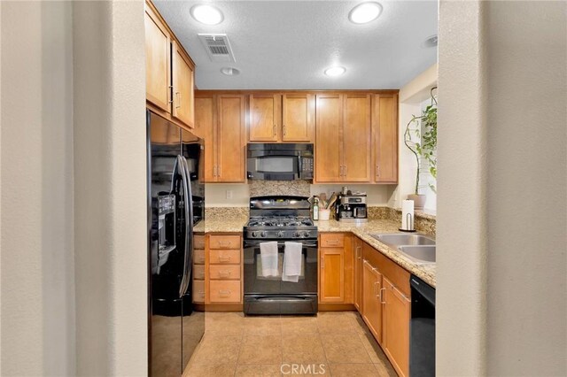 kitchen with light tile patterned flooring, light stone countertops, a textured ceiling, black appliances, and sink