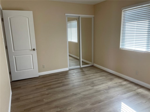 unfurnished bedroom with light wood-type flooring, a closet, and multiple windows