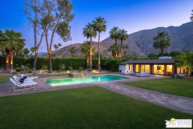 pool at dusk featuring a yard, outdoor lounge area, a mountain view, an in ground hot tub, and a patio