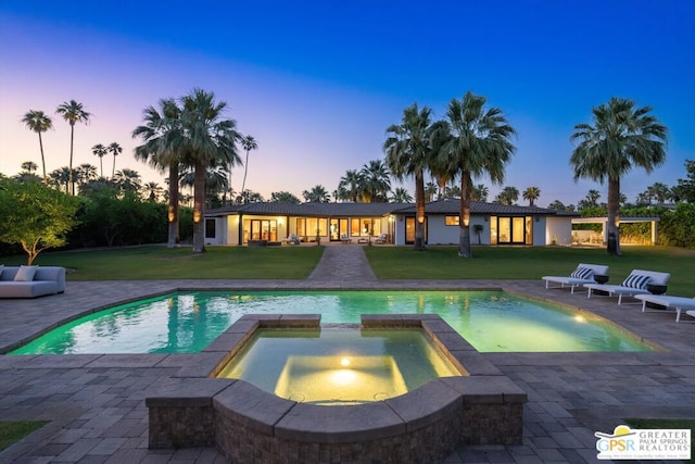 pool at dusk featuring a yard, outdoor lounge area, a patio, a mountain view, and an in ground hot tub