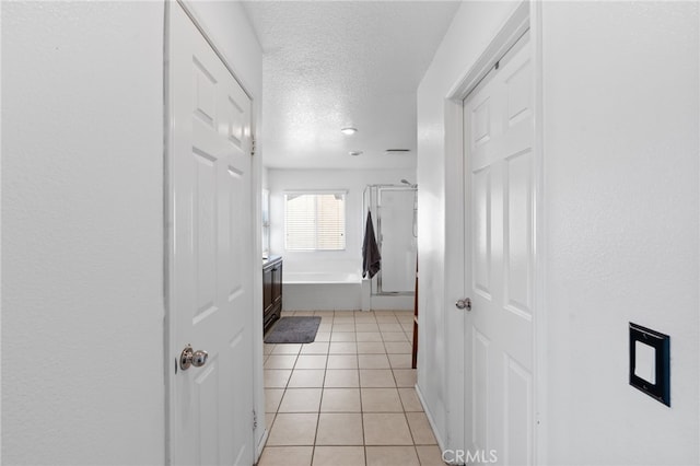 hall with a textured ceiling and light tile patterned floors